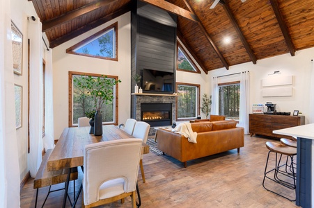 A spacious living room with wooden vaulted ceiling, large windows and a fireplace.