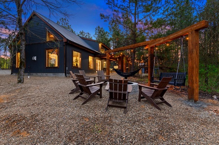 Modern cabin features outdoor seating with adirondack chairs around a fire pit, a hammock, and swings.