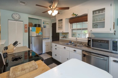 A tidy kitchen with white cabinets, stainless steel appliances, a ceiling fan, and a large window above the sink.