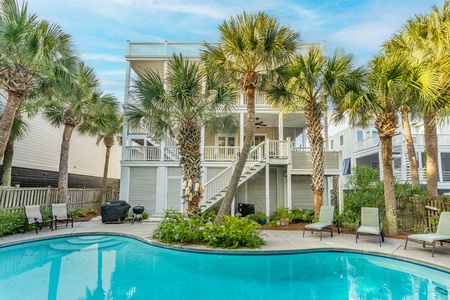 Staright view of the backyard facing the home and porches. Kidney shaped pool with plam trees.