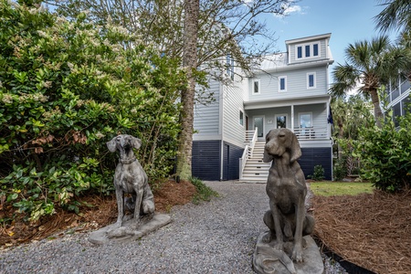 Two statues of a hound type dog frame a gravel walkway to the front of the home.