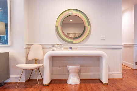 A modern room with a curved white desk, a white chair, a round mirror above the desk, and wooden flooring.