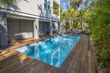 Modern house exterior with an illuminated pool and deck area, surrounded by trees and four grey lounge chairs.