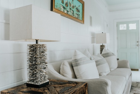 Beige sofa with striped cushions against a white shiplap wall, flanked by two stone-like lamps on wooden side tables, and a green door in the background.