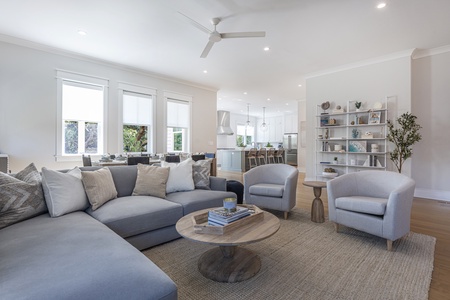 Grey sectional sofa on a natural woven rug with round wood coffee table and two grey sitting chairs.