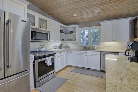 White kitchen cabinets with wood ceiling and floors, stainless steel appliances and a window over the sink.