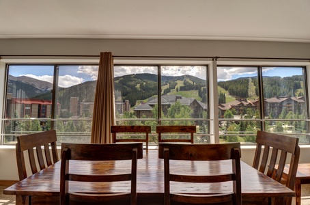 A dining table with chairs is adjacent to large windows looking out to the mountain.