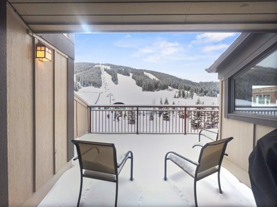 Two chairs on a snow-covered balcony facing a ski slope with ski lifts under a partly cloudy sky.