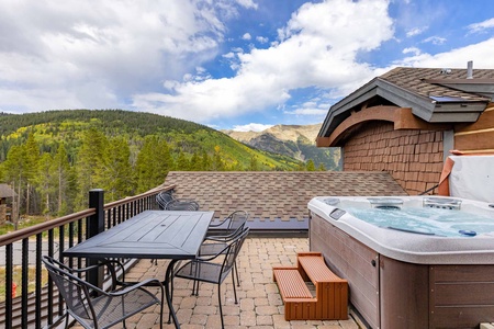 Outdoor patio featuring a table with seating, a hot tub, and a view of mountains.