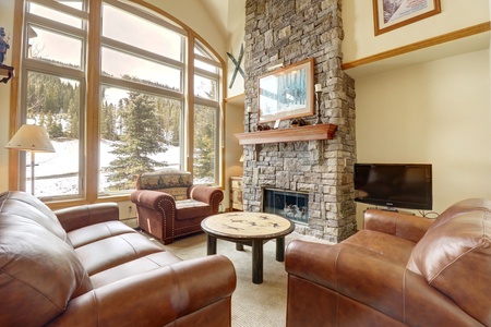 Open concept living room with tall ceilings, large windows allowing ample natural light in, stone fireplace, and multiple seating options.