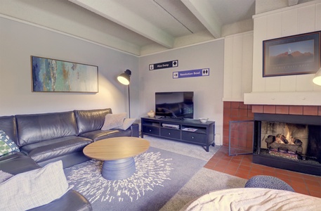 A cozy living room featuring a sectional sofa, a round coffee table, a TV on a media console, a fireplace, wall art, and directional signs on the wall.