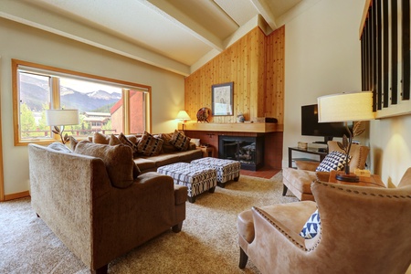 The living room has many seating options, a fireplace, and large picturesque window.