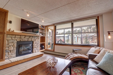 Cozy living room features a fireplace, large TV, and enclosed balcony area.