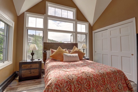 Bright master bedroom with cozy queen bed, tall ceilings and windows