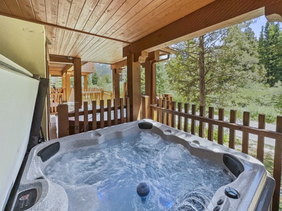 An outdoor hot tub on a wooden deck with bubbling water, surrounded by a wooden fence and trees in the background.