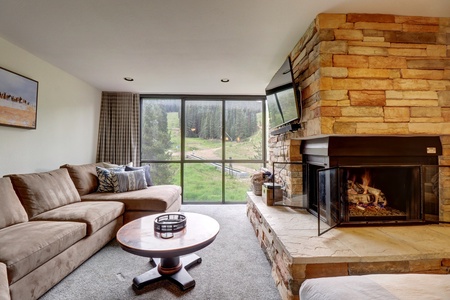 Living room space with large floor to ceiling windows and a cozy fireplace.