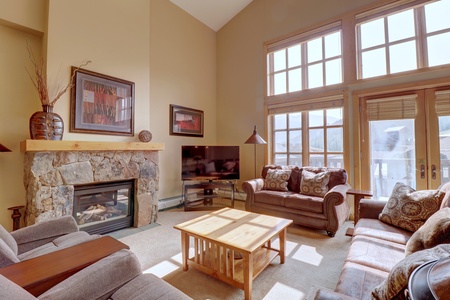 A bright living room features a stone fireplace, large windows, multiple seating options.