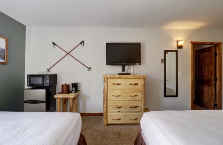 A hotel room with two queen beds looking at TV and dresser.