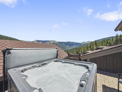 A rooftop hot tub with bubbling water overlooks a scenic mountain landscape under a clear blue sky.