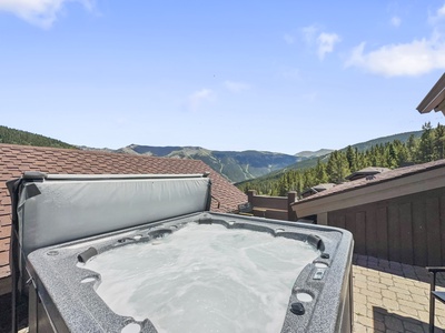 A rooftop hot tub with bubbling water overlooks a scenic mountain landscape under a clear blue sky.