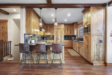 A modern kitchen with wooden cabinets, an island with barstools, pendant lighting, and stainless steel appliances.