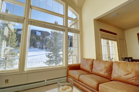 A cozy living room with a brown leather couch placed next to large windows offering views of Copper Mountain ski slopes.