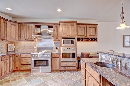 A kitchen with wooden cabinets, stainless steel appliances, a built-in microwave and oven, a modern faucet, and a tiled backsplash. The floor is covered with multi-colored tiles.