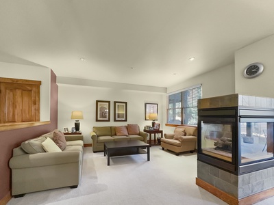 A living room with beige walls featuring two couches, a coffee table, two framed pictures, lamps, and a fireplace with a clock above it.