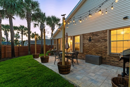Private patio with string lights, palm trees, and outdoor dining—perfect for relaxing evenings and al fresco meals in a fenced backyard oasis.