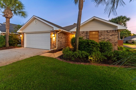 Charming brick home with lush landscaping and warm exterior lighting—welcoming curb appeal for a relaxing coastal getaway.