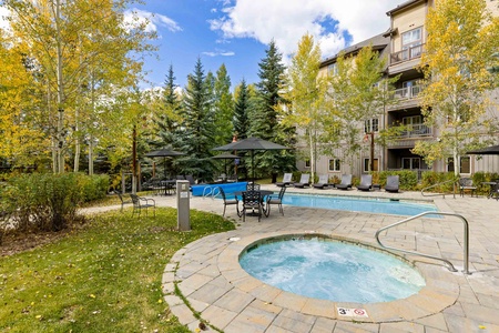 Outdoor area of a residential complex featuring a swimming pool, hot tub, lounge chairs, and surrounding trees.