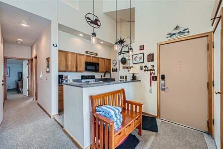 A cozy entrance hallway with a wooden bench, adjoining a kitchen with wooden cabinets and a breakfast bar. Various decorations adorn the walls, and a door is visible to the right.