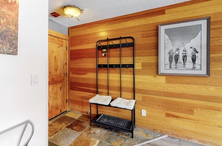 Wood-paneled entryway with a black metal coat rack, white cushioned bench, and framed black-and-white photo on the wall.