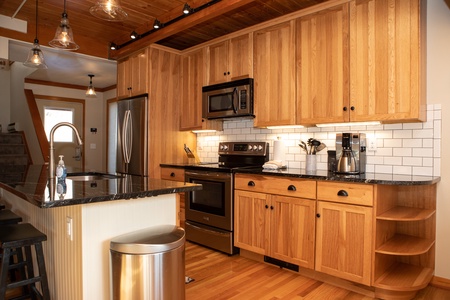 A modern kitchen with wooden cabinets, stainless steel appliances including a refrigerator, stove, and microwave, a black granite countertop, and a white subway tile backsplash.