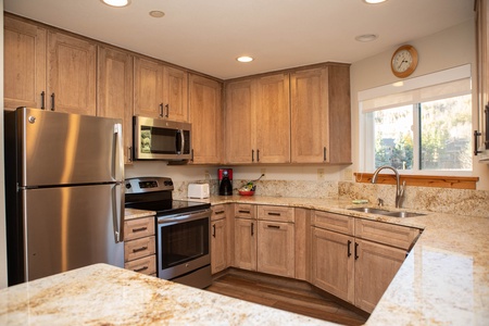 A modern kitchen with wooden cabinets, stainless steel appliances, granite countertops, and a window above the sink.