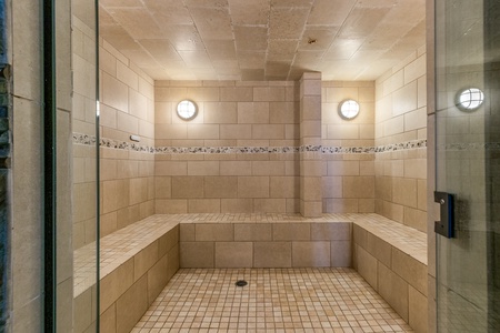 A tiled steam room with bench seating, recessed lighting, and a glass door.