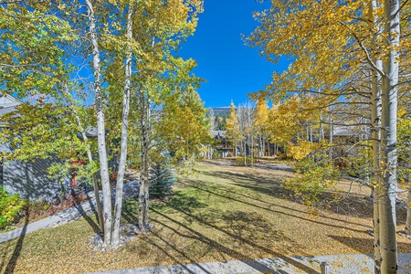 A serene autumn landscape with trees shedding yellow leaves, a grassy area, and clear blue sky in the background.