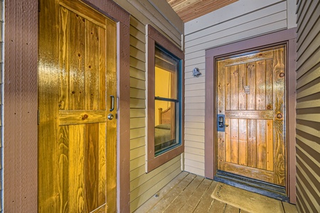 A narrow porch features two closed wooden doors—one on the left and one straight ahead—each framed with brown trim. A small lit window is situated between the doors. The floor is wooden planks.