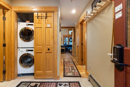 A hallway in a home featuring wooden doors, a stacked washer and dryer in a closet, and carpets with bear patterns. A door with a keypad lock is on the right.