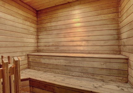 A wooden sauna interior with bench seating along the walls, illuminated by warm overhead lighting.