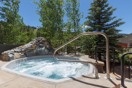 Outdoor hot tub surrounded by trees and mountains, featuring a metal handrail and bubbling water.