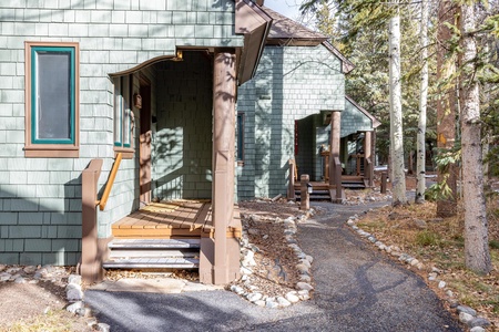 Pathway leading to the entrance of multiple green wooden cabins nestled among trees in a forested area.