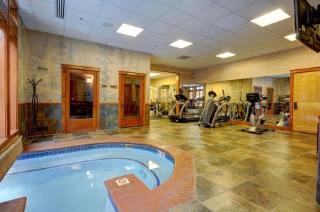 Image of a fitness center with exercise equipment, a sauna, and a small indoor pool. The room has tiled flooring and wooden decor elements.