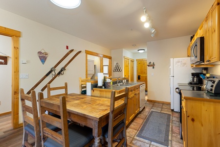 A cozy, rustic kitchen with wooden cabinets, an island, a dining table with chairs, modern appliances, and a hallway leading to additional rooms.