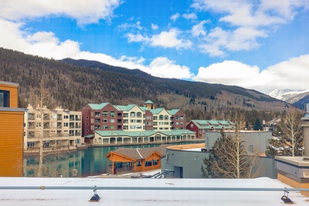 Scenic view of a mountainous resort area with buildings around a lake and snow-covered landscapes under a partly cloudy sky.