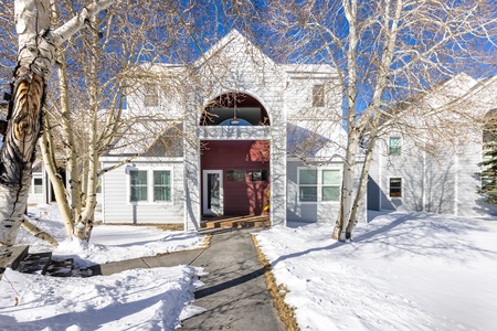 A white, two-story residential building with a central passage and bare trees in a snowy landscape.