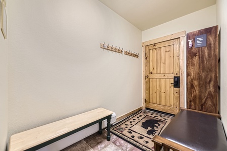 Entryway with wooden door, coat hooks on the wall, a bench, and a decorative rug featuring a bear design.