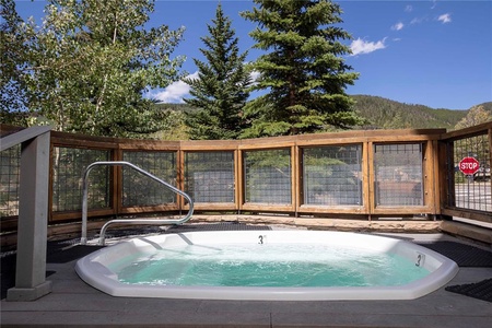 A circular outdoor hot tub surrounded by a wooden fence with trees and mountains in the background. A stop sign is visible on the right side.