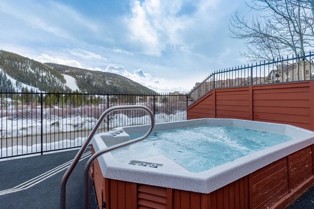 Outdoor hot tub with water jets running, situated on a fenced deck overlooking a snowy mountainous landscape.