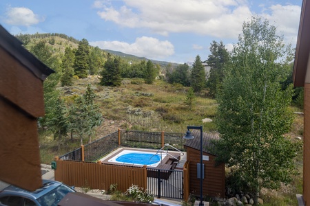 View of a small fenced pool surrounded by trees, with mountains in the background under a partly cloudy sky.